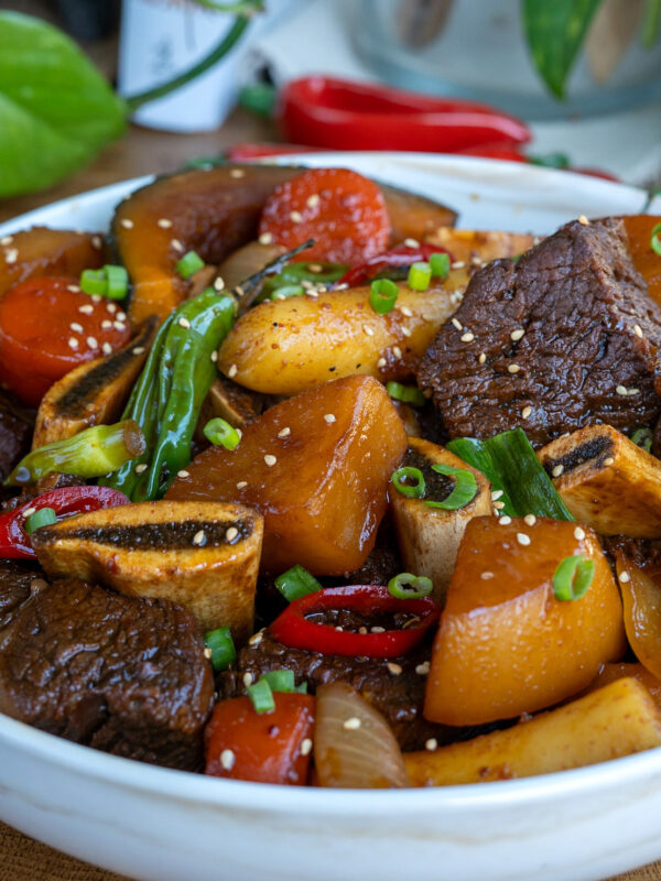 a bowl of galbi jjim (koran braised short ribs) with korean radish, peppers, carrots, and rice cake.