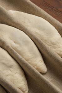 Four pieces of dough proofing on brown bakers couche, ready for baking.