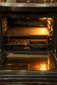 The image shows an open oven with a baking steel on the top rack and a cast iron pan on the bottom of the oven.