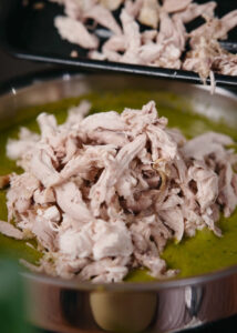 Shredded chicken piled on a green salsa in a saute pan