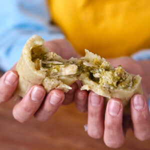 A green chicken tamale pulled apart to show the texture of the moist masa and fillings.