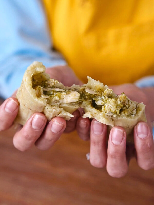 A green chicken tamale pulled apart to show the texture of the moist masa and fillings.