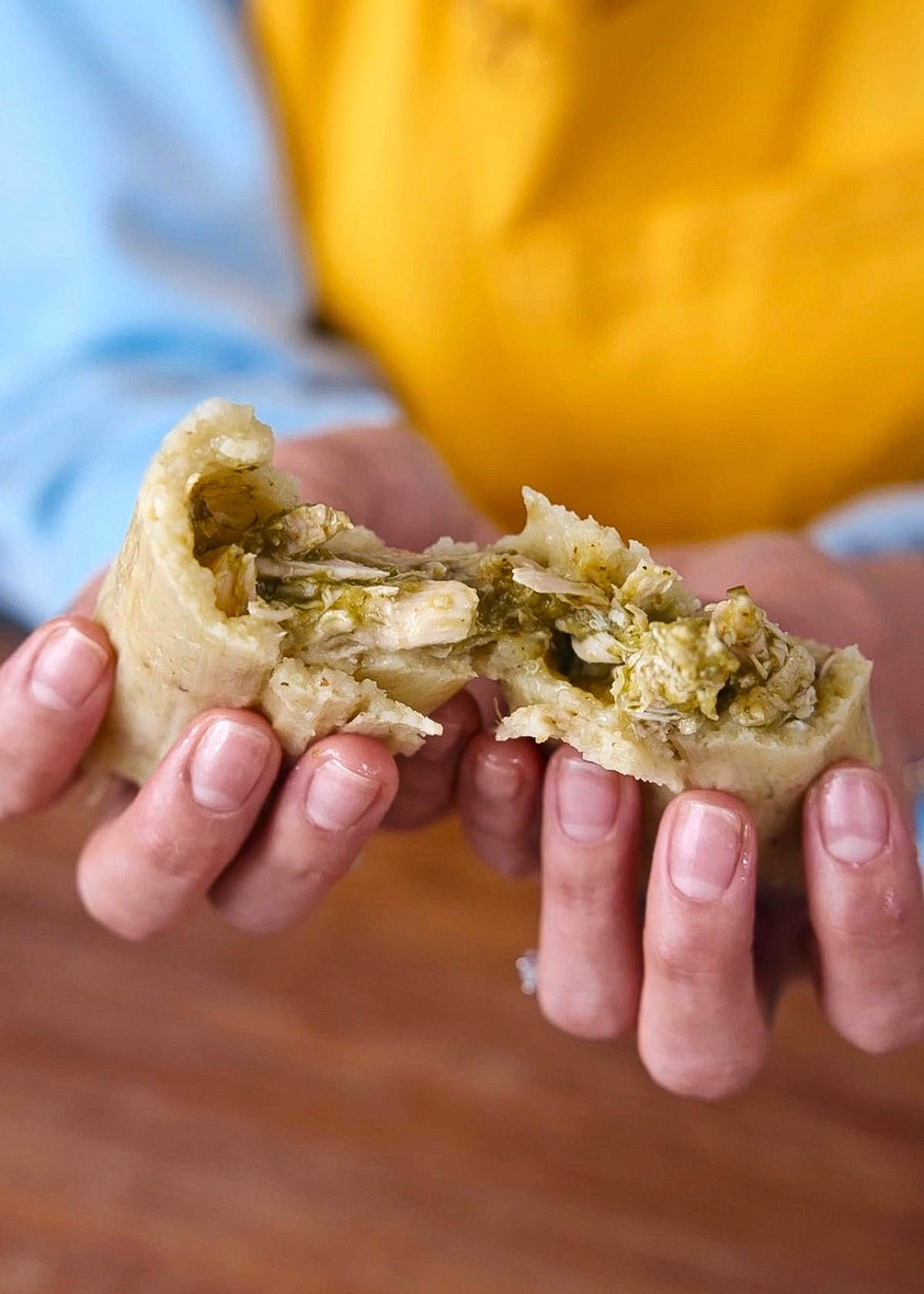 A green chicken tamale pulled apart to show the texture of the moist masa and fillings.