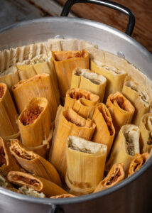 A large pot filled with neatly arranged tamales, wrapped in corn husks. The tamales vary in color, indicating different fillings.