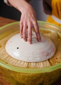 corn husks soaking in water with a pot lid to weight it down.