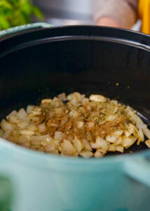 a pot with translucent onions and garlic, topped with some seasonings