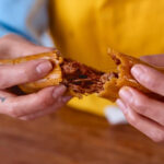 Two hands breaking apart a tamale, revealing its shredded beef in red chile sauce filling. The masa is very moist, with a beef to masa ratio of about 2:1