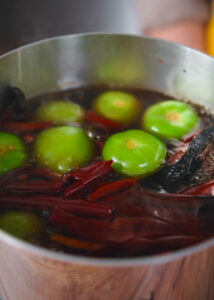 A pot filled with green tomatillos and red dried chili peppers boiling in pork broth