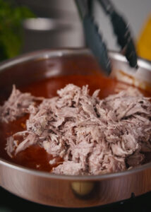 Shredded pork meat being mixed into the fried salsa roja