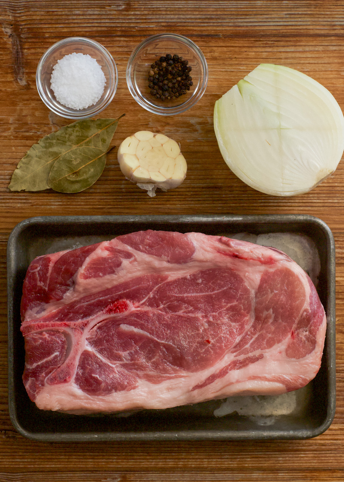 Raw bone-in pork butt, onion, black peppercorns, bay leaves, salt, and half a head of garlic.