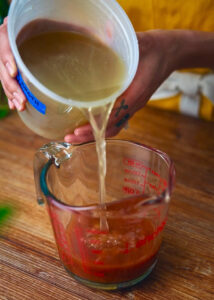 Warm pork broth with the fat skimmed off, being poured into a measuring glass with salsa roja.