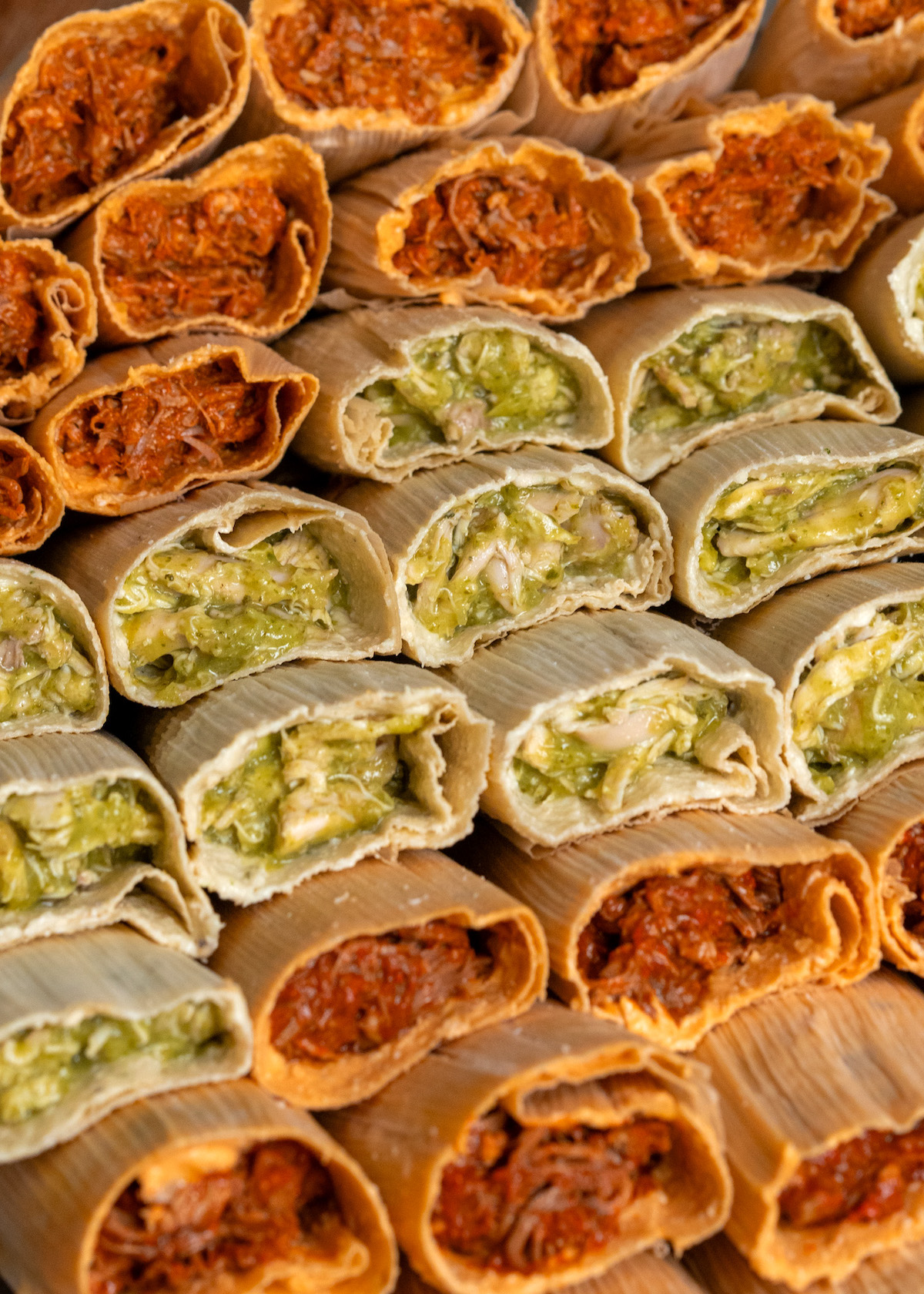 A close-up of a platter filled with a variety of tamales, green and red.