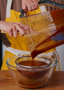 pouring salsa roja from a large measuring pitcher through a fine mesh strainer