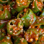 slice korean peppers coated in a sweet ssamjang sauce and sprinkled with sesame seeds. The peppers are arranged in a heap, showcasing their vibrant color and texture.