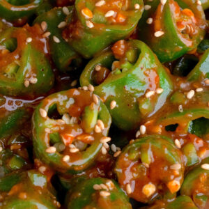 Close-up of sliced korean peppers coated in a sweet ssamjang sauce and sprinkled with sesame seeds. The peppers are arranged in a heap, showcasing their vibrant color and texture.