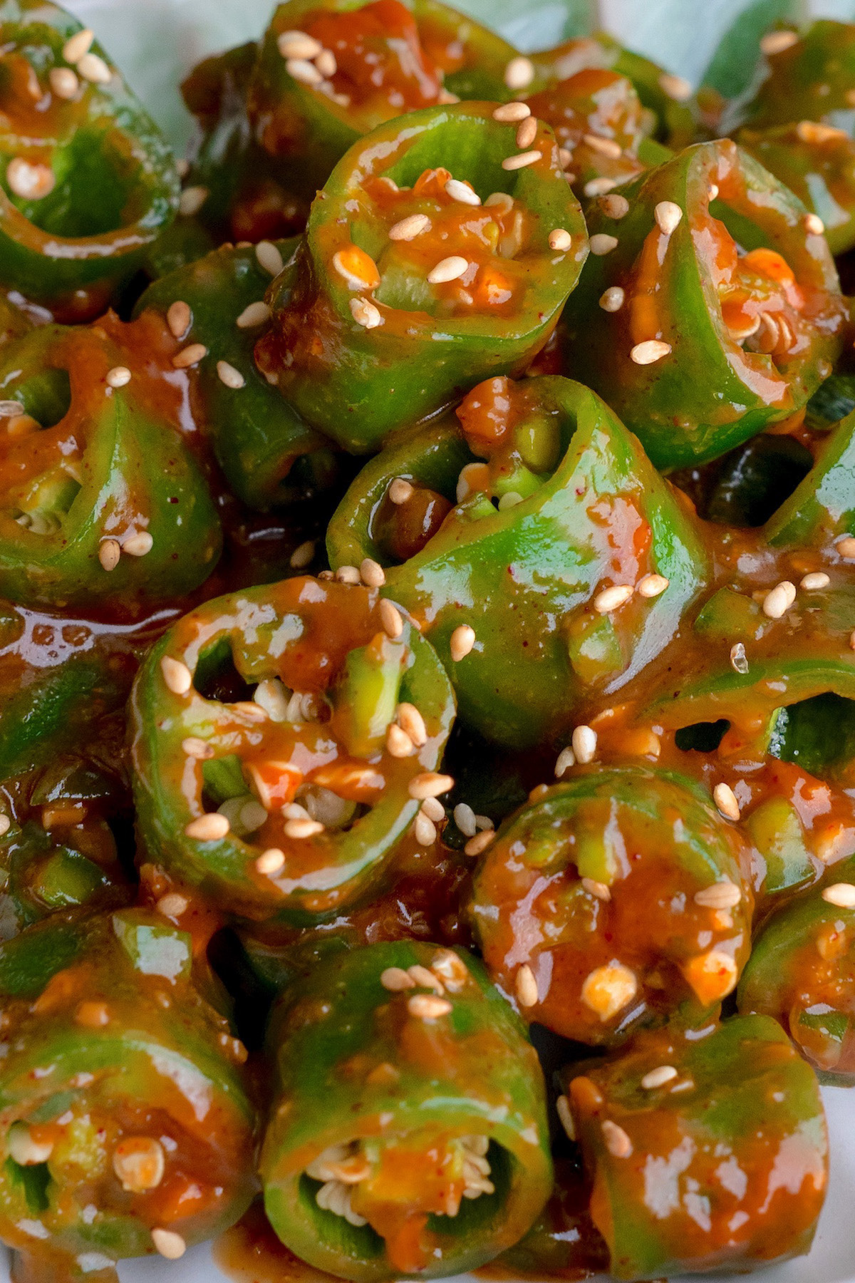 Close-up of sliced korean peppers coated in a sweet ssamjang sauce and sprinkled with sesame seeds. The peppers are arranged in a heap, showcasing their vibrant color and texture.