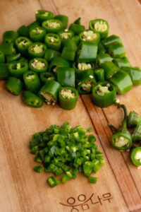 Chopped korean chili peppers rest on a wooden cutting board, along with a diced jalapeno