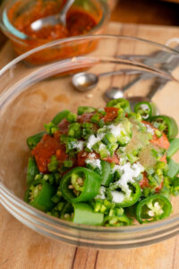 A glass bowl filled with sliced korean peppers, sugar, ssamjang, minced jalapenos, and sesame oil